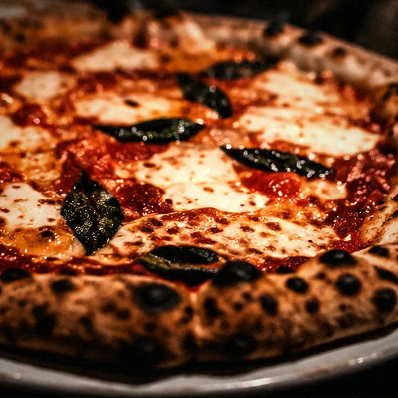 Eine ganze Pizza mit Mozzarella, Tomatensauce und Basilikum auf einem Teller